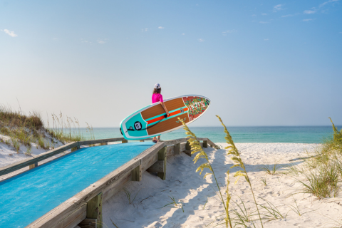 A person holding a surfboard on a wooden boardwalk.