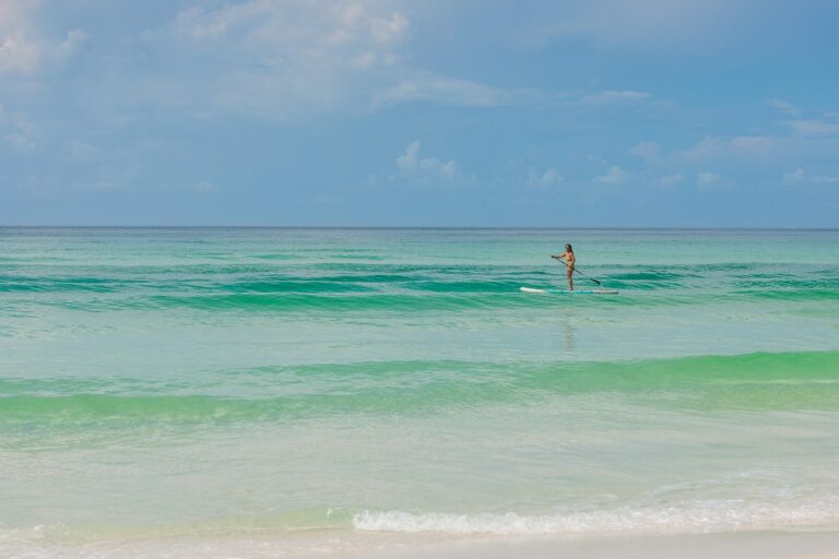 A person paddleboarding on calm turquoise ocean waters under a partly cloudy sky.