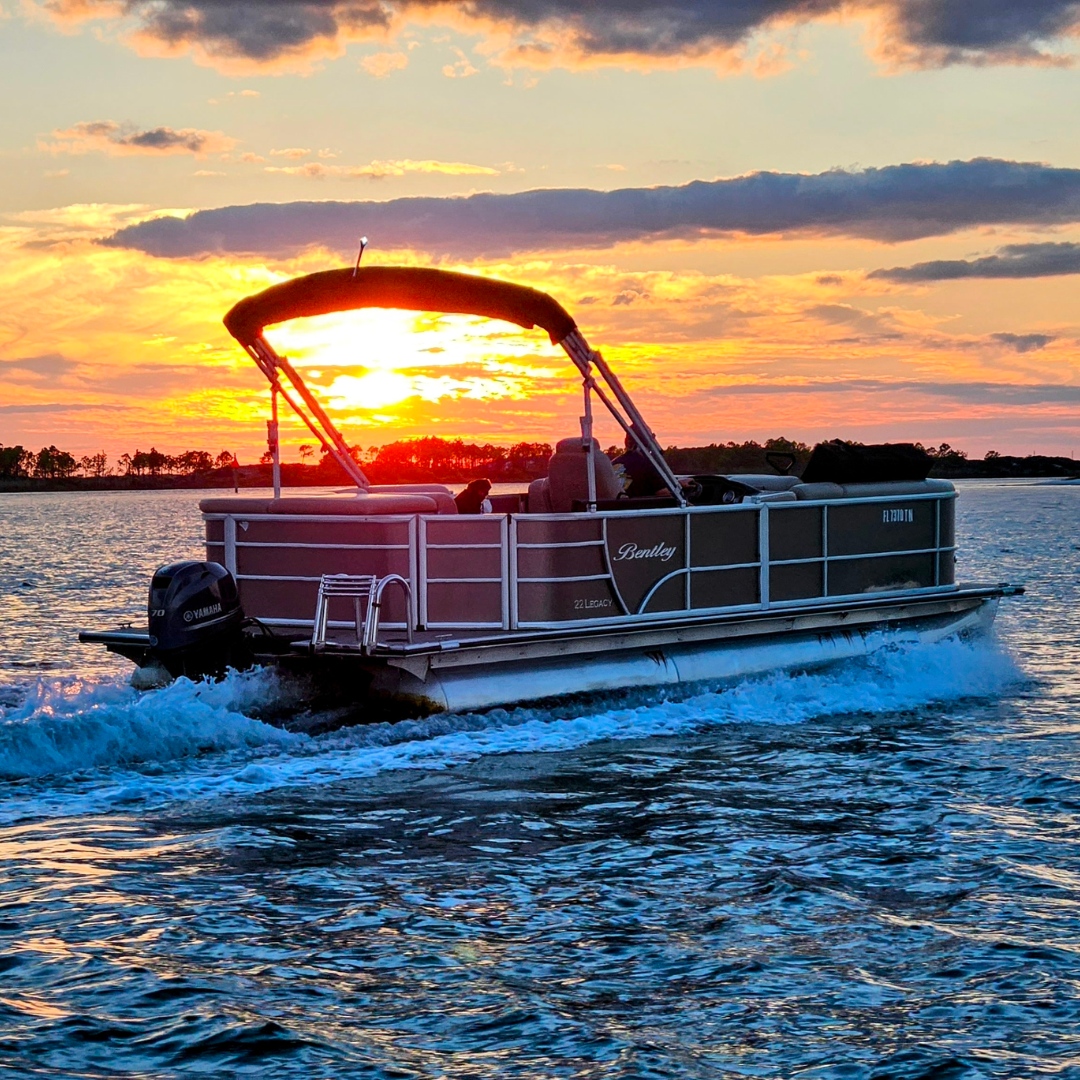 Pontoon boat cruising on a lake at sunset, with a vibrant sky and water reflecting the warm colors.