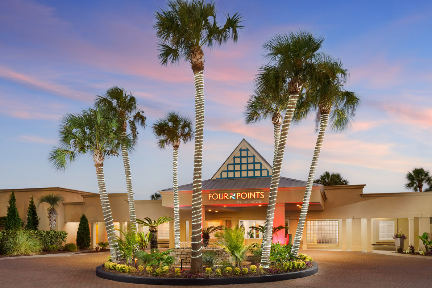 Entrance of a hotel with palm trees and a pyramid-shaped roof. Sign reads 