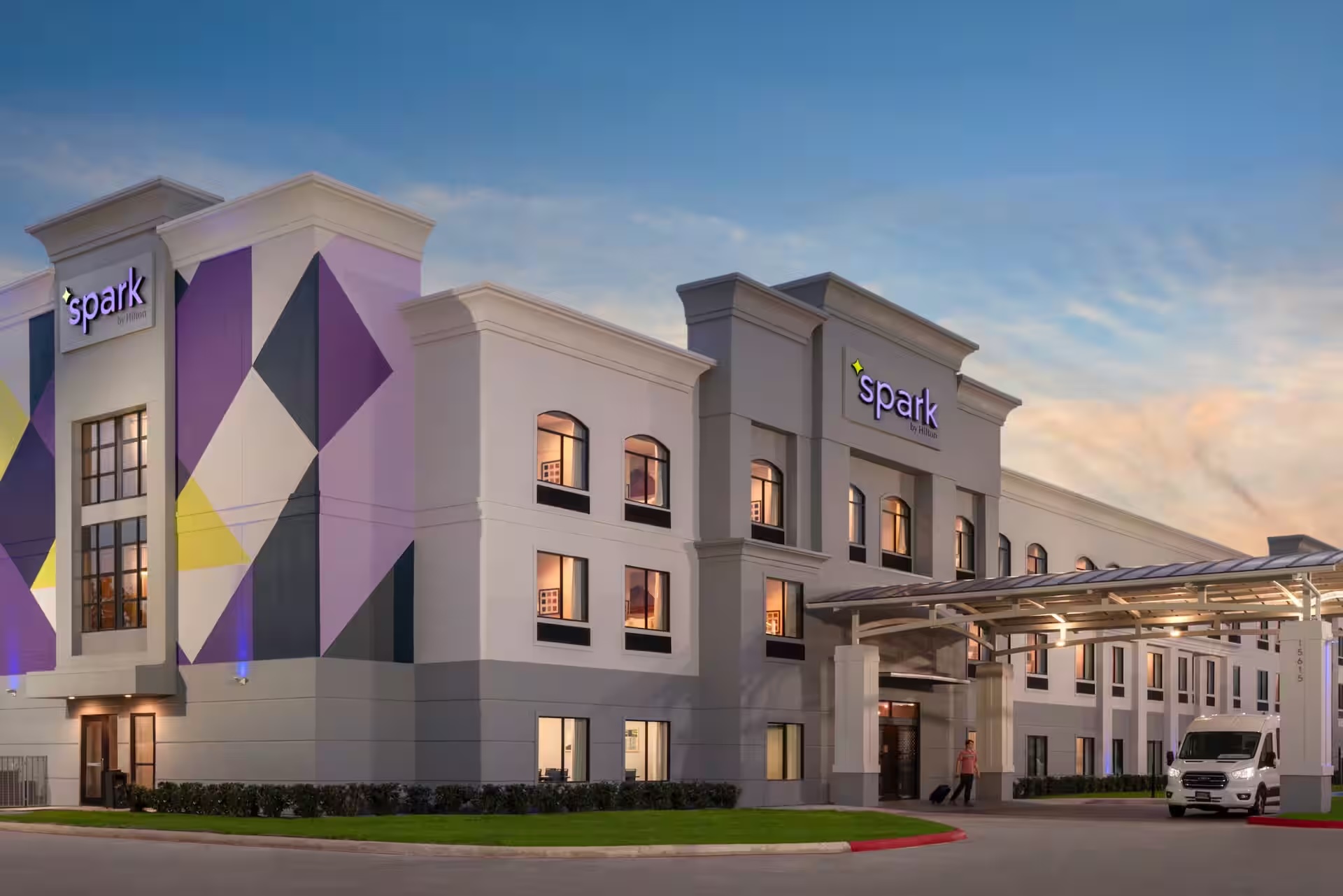 A modern hotel exterior featuring geometric designs and a prominent entrance, with a parked shuttle van nearby at sunset.