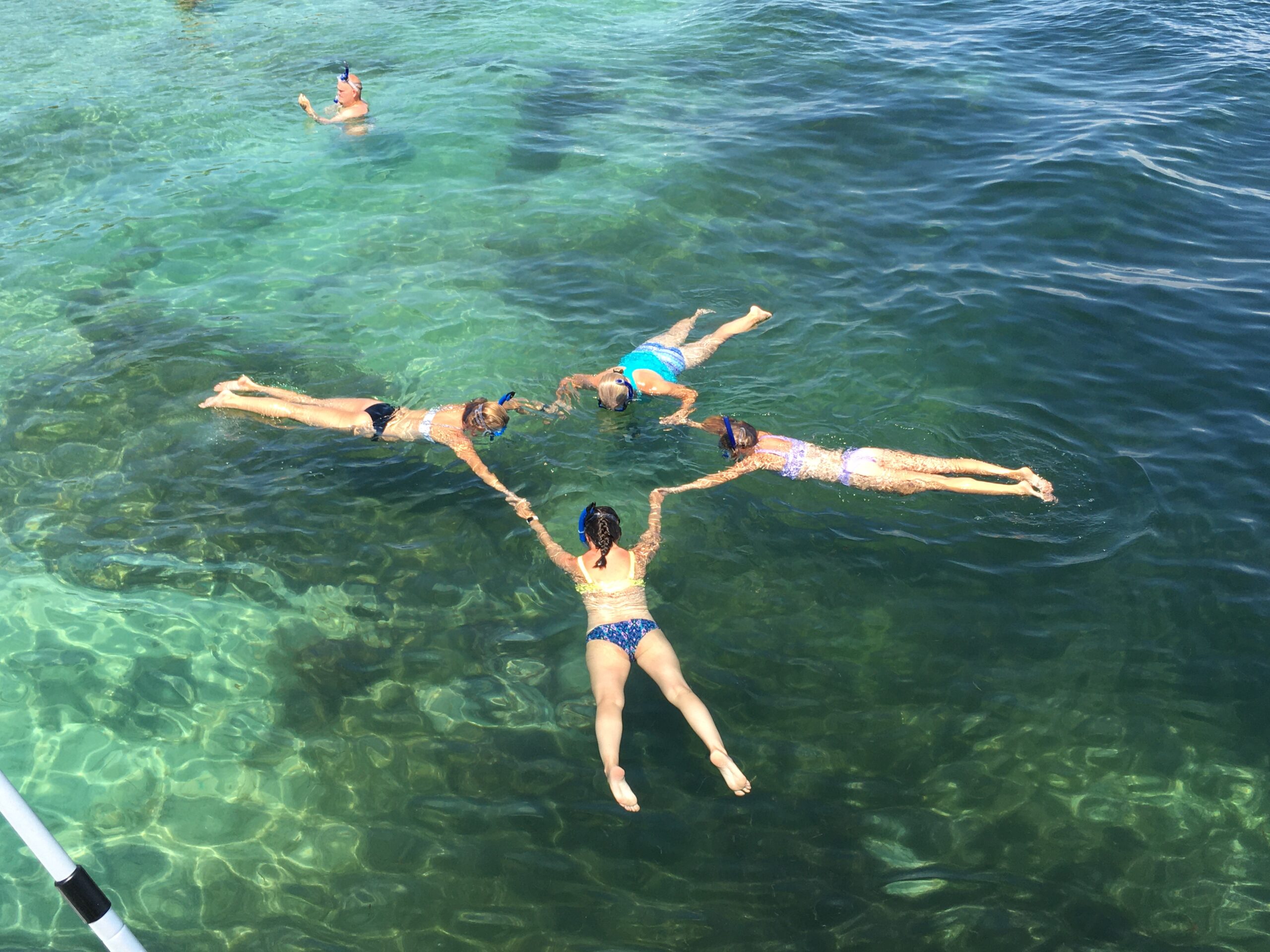 Five people are floating on their backs in a star formation in clear turquoise water.